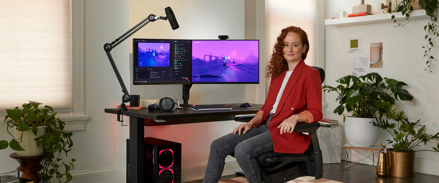 Foto af Dr. Lindsey Migliore siddende i en Embody gaming-stol vendt mod kameraet med Nevi gaming-skrivebord i sort med ollin-skærmarme