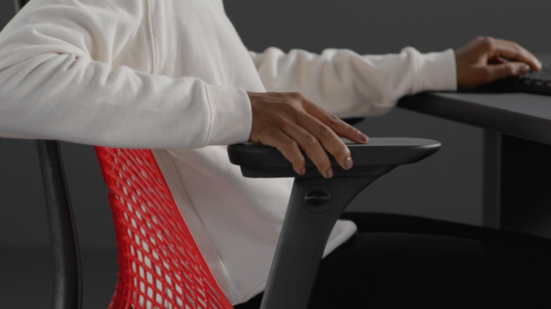 En video af en person, der sidder i en rød og sort Sayl-gamingstol fra Herman Miller og rækker ud efter stolen for at justere armene.