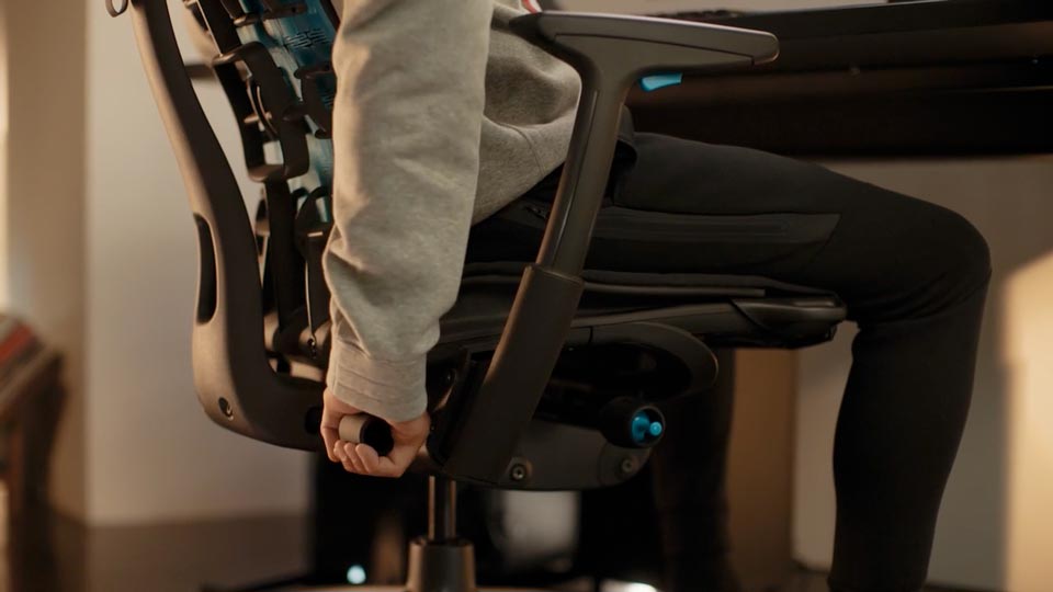 En video af en person, der sidder i en sort og blå Embody-gamingstol fra Herman Miller, og rækker om bag stolen for at justere rygstøtten.