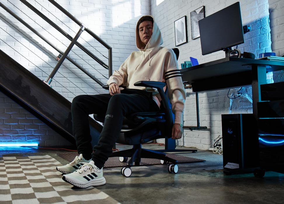Billede af Jelty fra G2 Esports-teamet siddende i G2 Embody-stolen med ryggen til gaming-opsætningen, herunder Nevi-gamingbord i sort med Ollin-skærme