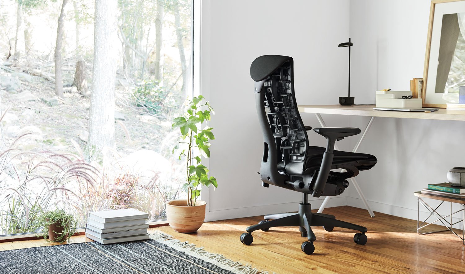 En sort Embody-kontorstol fra Herman Miller i et indendørs miljø. Rummet indeholder elementer som møbler, gulvbelægning og dekorative genstande som en urtepotte og en vase.