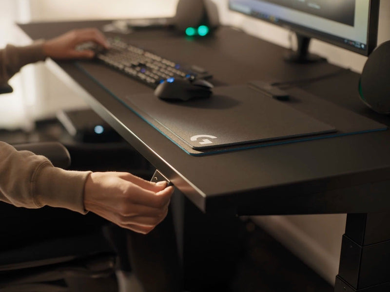 En video af en person, der sidder ved et sort Nevi-gamingskrivebord fra Herman Miller og trykker på en knap for at sænke skrivebordet.