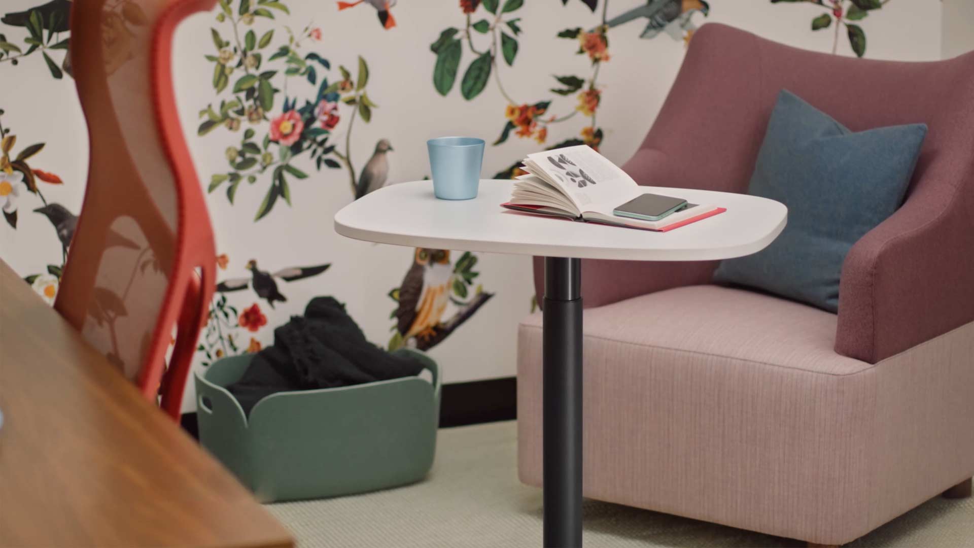 En video af en kvinde, der sidder i en gul Wilkes-lænestol og bruger et Passport-bord fra Herman Miller. Videoen viser fortsat, at Passport-bordet bruges flere steder, både på kontorer og i hjemmet.