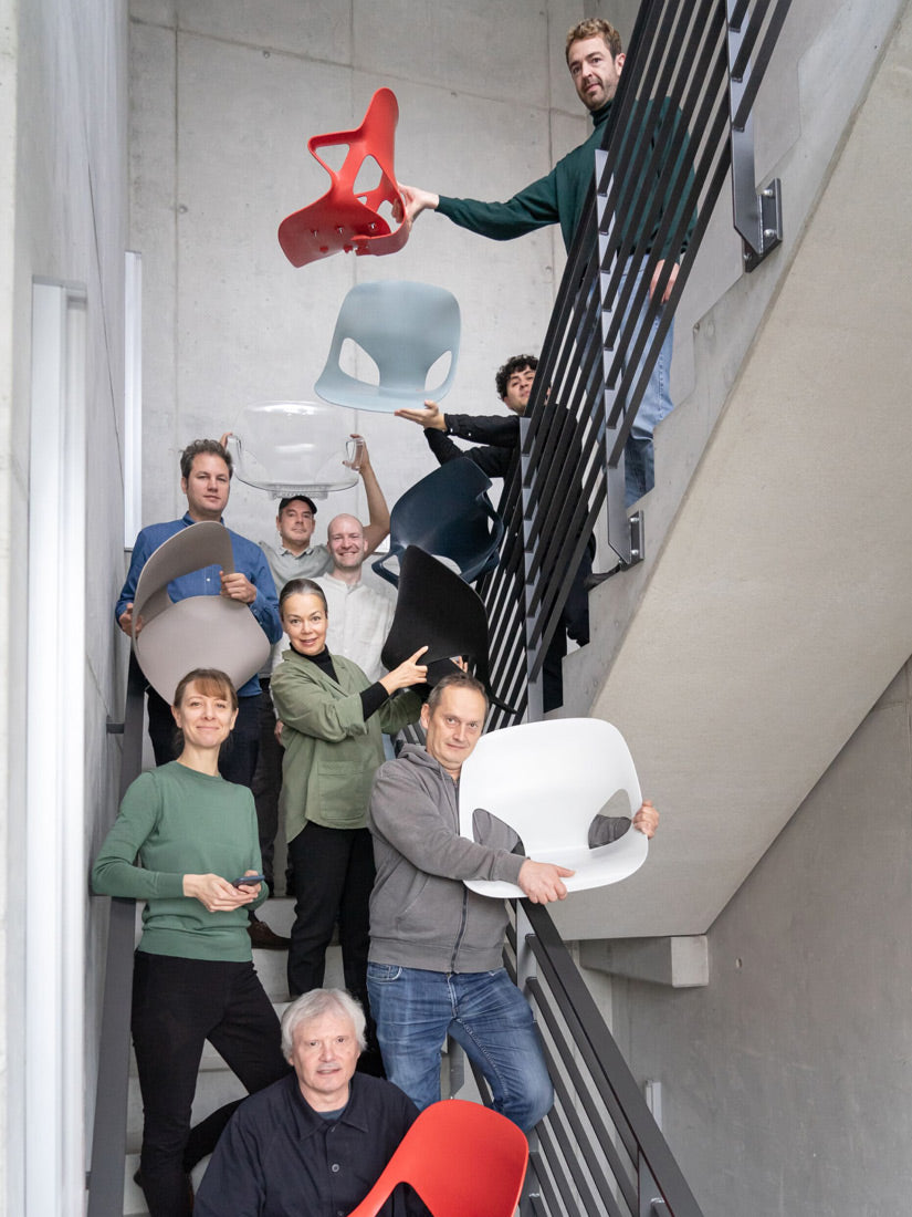 Foto af medlemmer af Studio 7.5-designteamet i en trappeopgang, hvor nogle holder forskellige dele af Herman Zeph-stolen, som de har designet