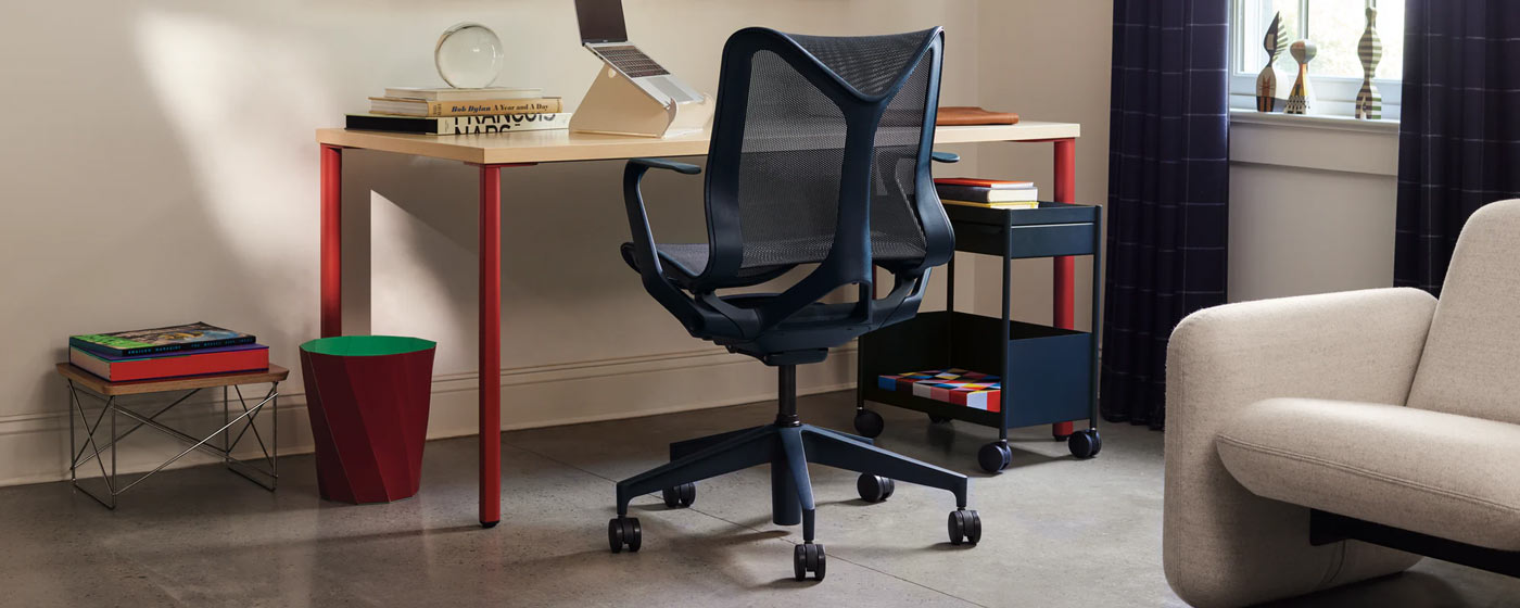 En blå Cosm-kontorstol fra Herman Miller, placeret foran et rødt og asketræs OE1-skrivebord fra Herman Miller. Placeret i et hjemmekontor, tilbehør med en blå OE1-vogn, hvid Oripura-laptopstativ og rød HAY Paper-papirkurv.