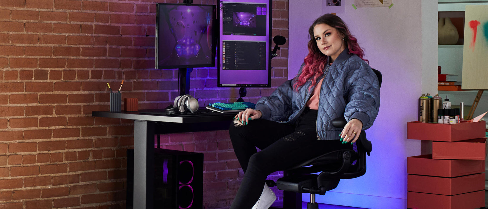 Foto af gamer Electra vendt mod kameraet siddende på Aeron gaming onyx black foran Nevi gaming-skrivebord i sort med Ollin-skærm