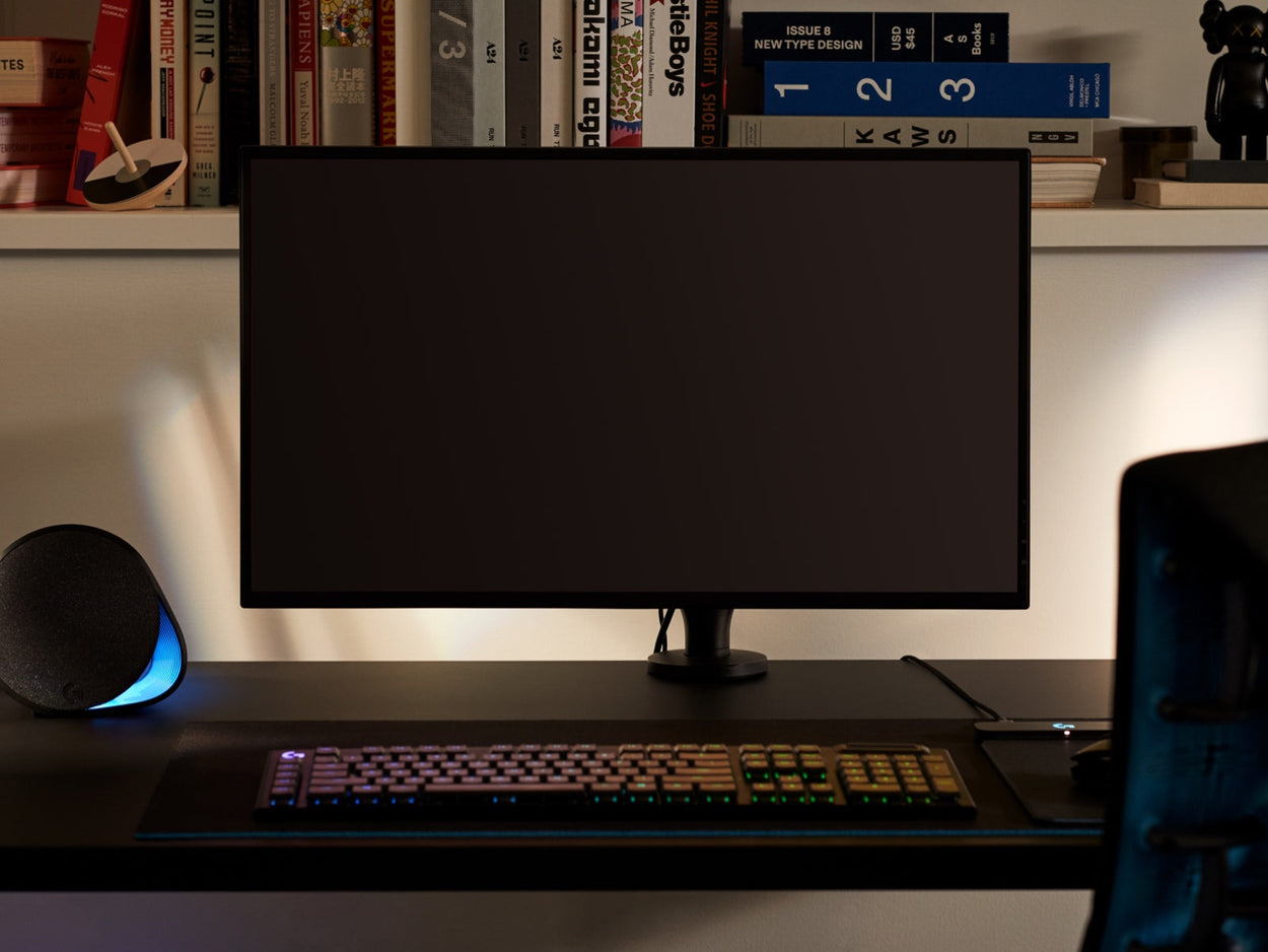 Frontbillede af en sort Ollin-skærmarm, der holder en computerskærm og er fastgjort til et sort Nevi-gamingbord fra Herman Miller. Opstillet i et spillerum eller hjemmekontor med en bogreol, tastatur og mus.