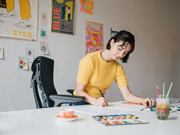 Illustrator, maler og forfatter Molly Rose Dyson arbejder i sit atelier, siddende i en Embody-gamingstol i sort og cyanblå