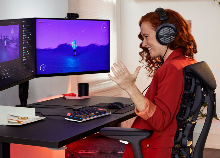 Foto af Dr. Lindsey Migliore, der smiler, mens hun spiller computerspil i Embody cyan gaming-stol med Nevi gaming-bord i sort