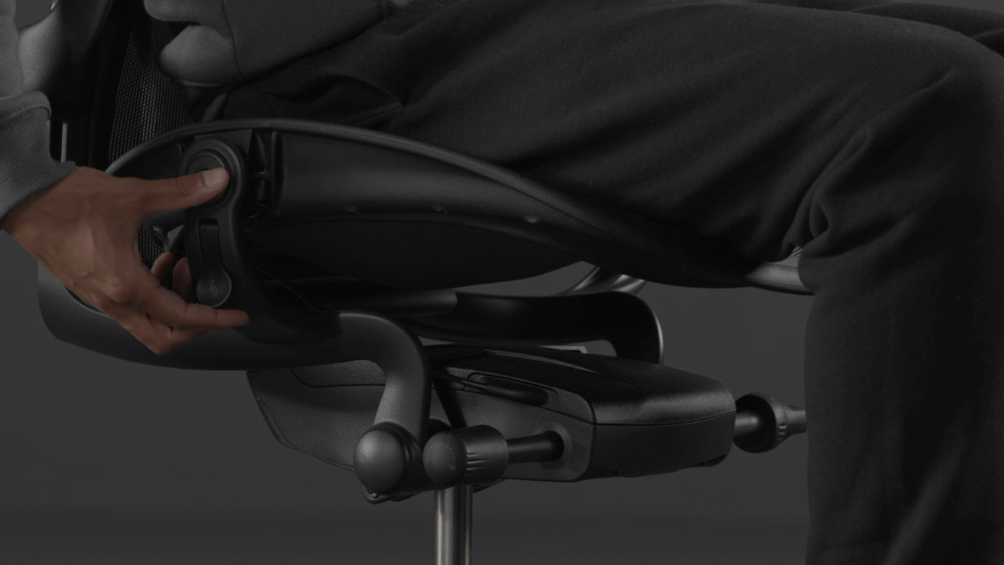 En video af en person, der sidder i en sort Aeron-gamingstol fra Herman Miller og rækker ud efter stolen for at justere sædehøjden.