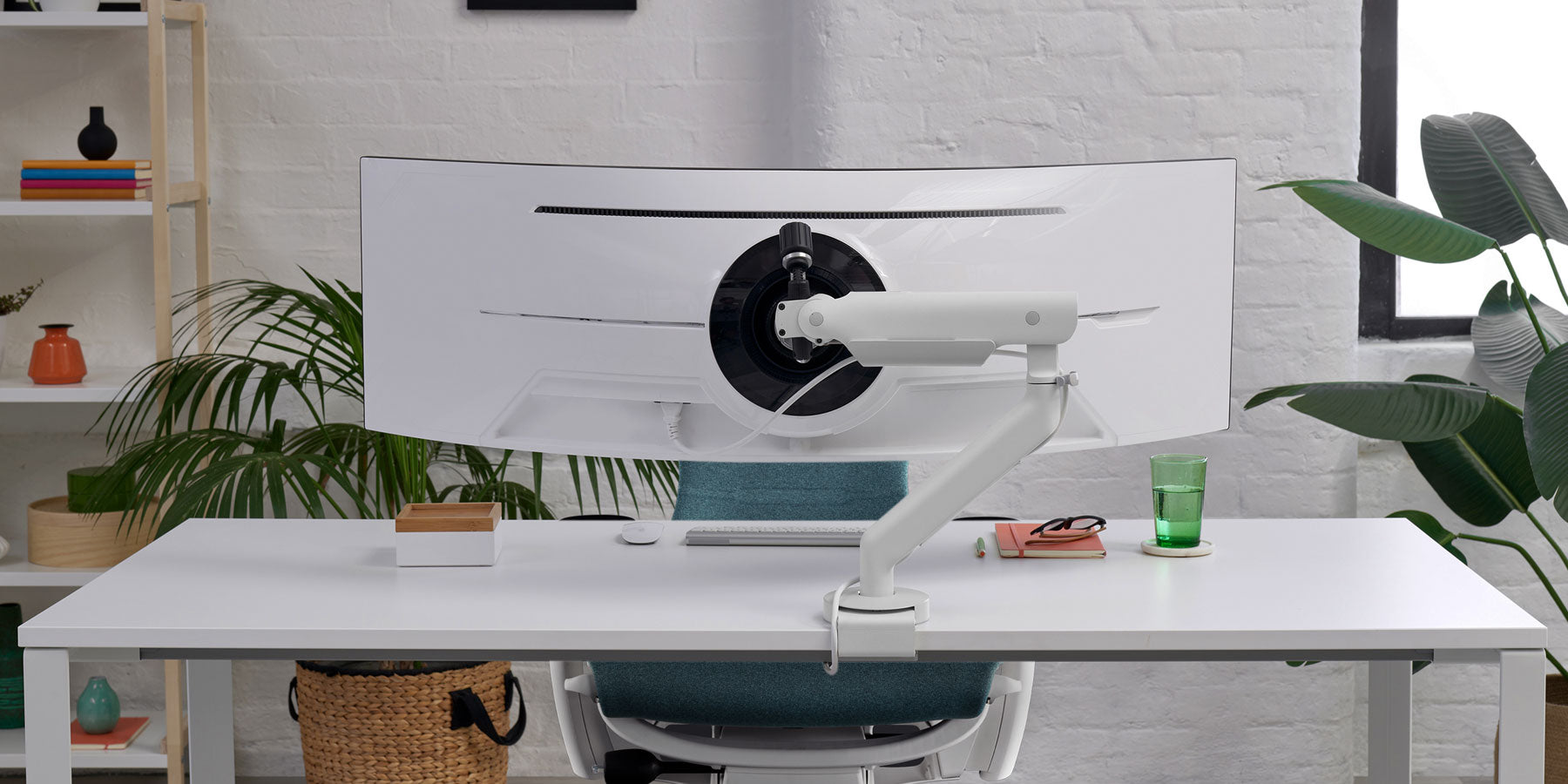 Frontbillede af en hvid Flo X-monitorarm fra CBS, der er fastgjort til et hvidt skrivebord foran en sort Aeron-kontorstol fra Herman Miller.