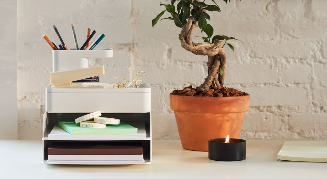 Et sæt grå Formwork-skrivebordsaccessories ved siden af en plante og et lys på et skrivebord.