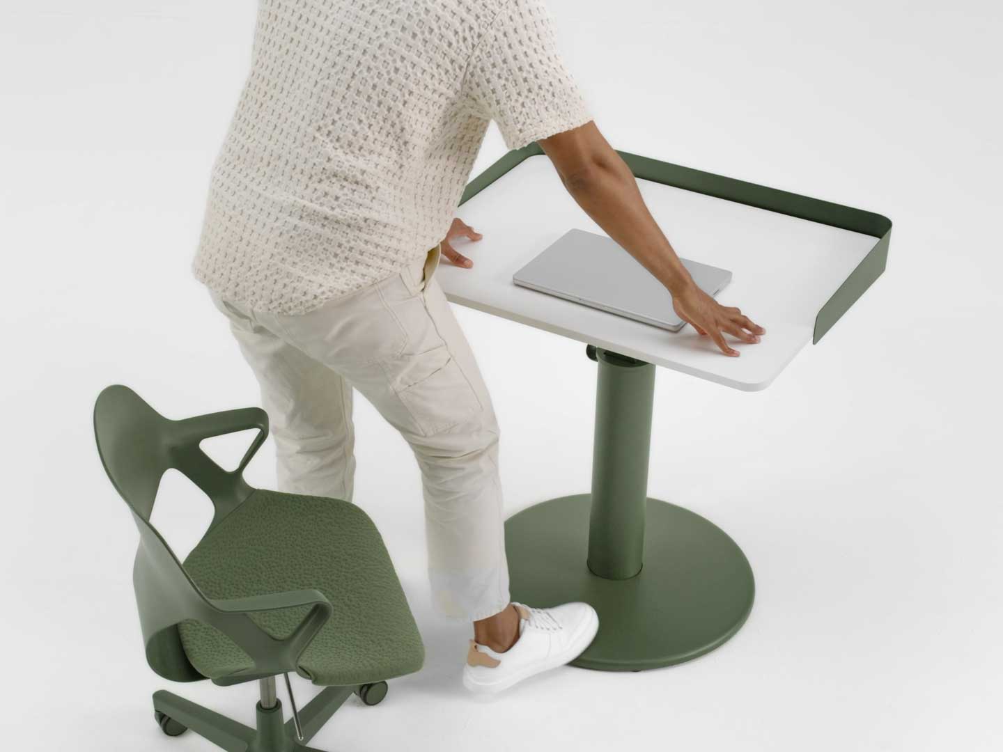 En video af en mand, der står op fra en grøn Zeph-stol fra Herman Miller og hæver højden på et grønt og hvidt OE1-stående skrivebord fra Herman Miller ved hjælp af sin fod.