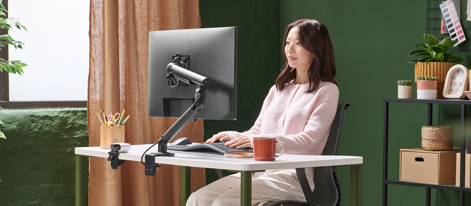 En kvinde sad ved et Herman Miller OE1-skrivebord og arbejdede ved en skærm, der var monteret på en sort Flo-skærmarm.
