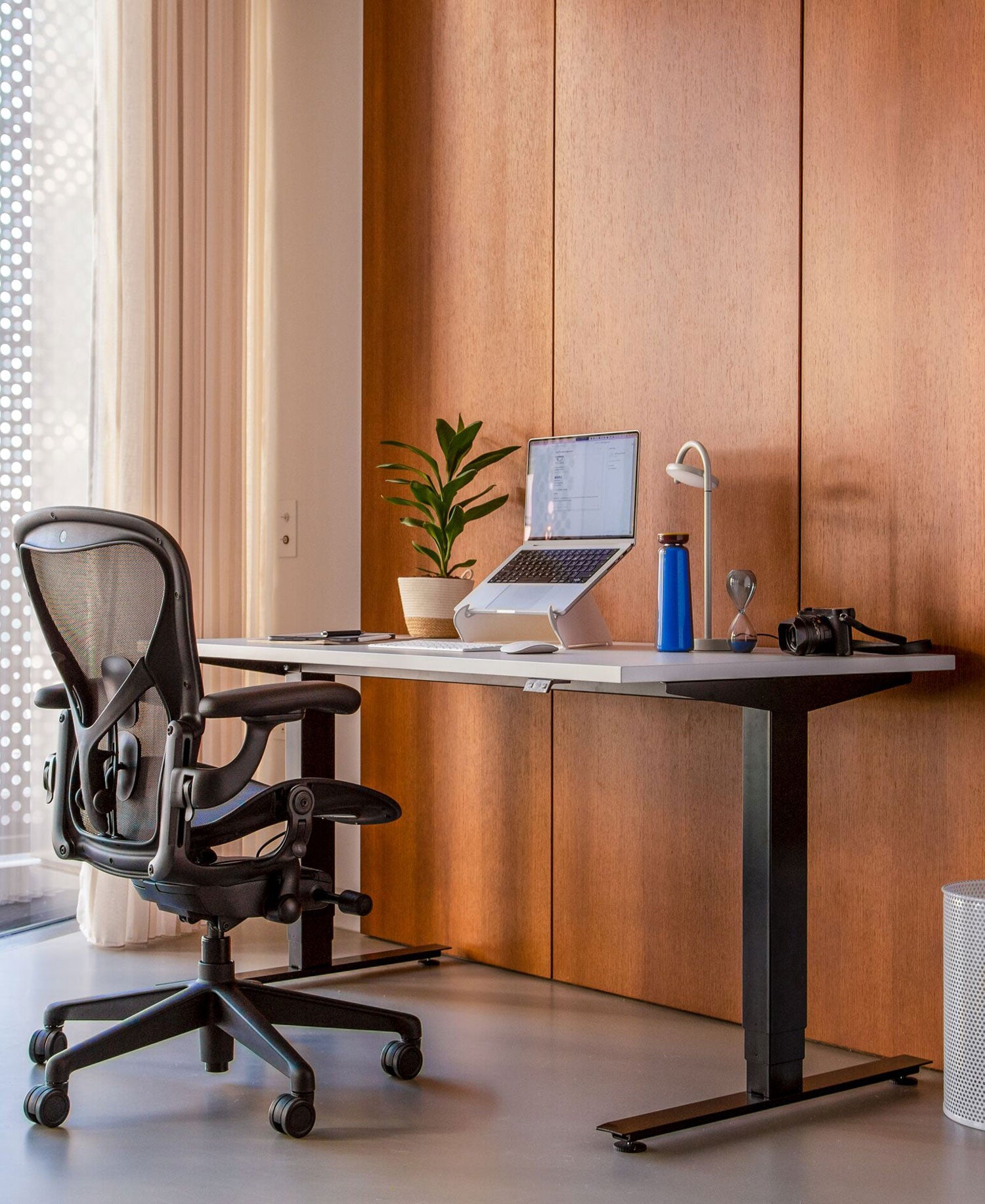 Hjemmekontor med Aeron-kontorstol i grafit foran Nevi-siddestativ med sorte ben og hvid bordplade og Oripura-laptopstativ.