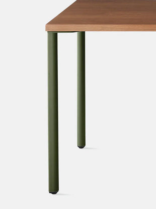 Nærbillede forfra af et grønt OE1-skrivebord i valnød fra Herman Miller, der viser det dråbeformede ben-design.