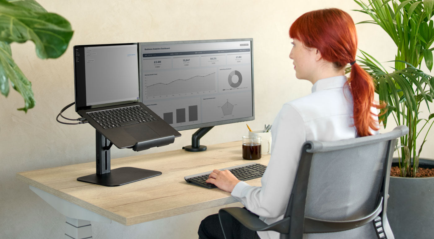 En dame, der bruger et hjemmekontor med et Nevi-skrivebord, Setu-stol og Lana-laptopstativ.