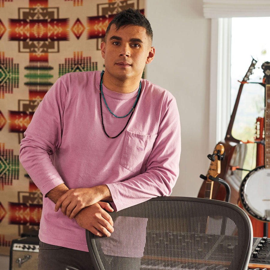 Foto af Rostam, musiker, producer og komponist, stående lænet op ad en Aeron-kontorstol i grafit med musikinstrumenter i baggrunden