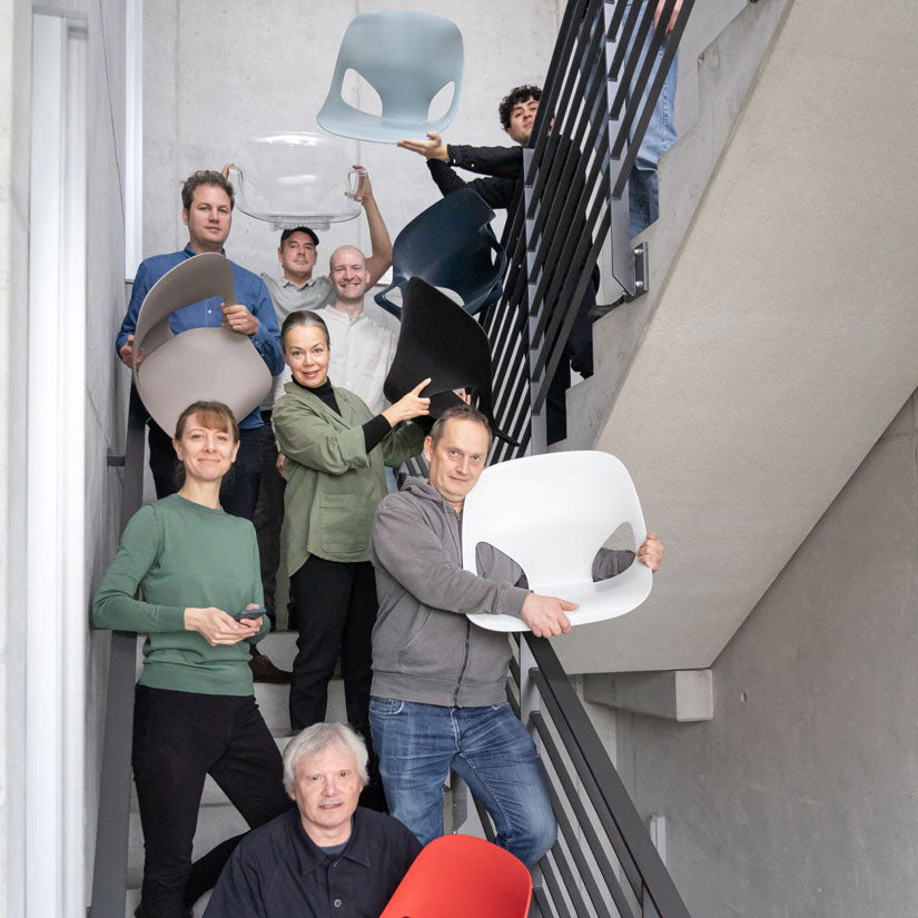 Fotografi af medlemmer af Studio 7.5-designteamet i en trappeopgang, hvor nogle holder forskellige dele af den Herman Zeph-stol, de har designet