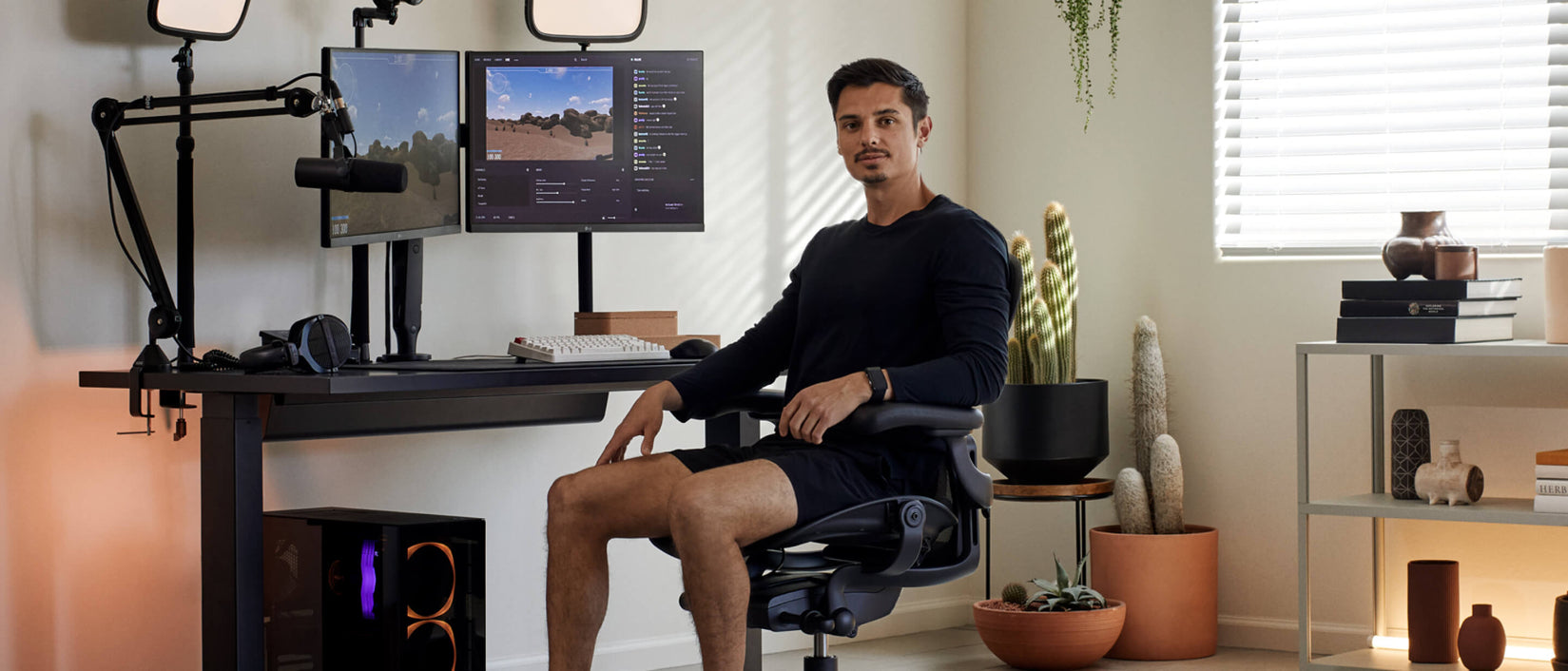 Billede af gamer Xaryu siddende med ansigtet mod kameraet i Aeron-gamingstol i grafit med gaming-opsætning bag sig med Nevi-gamingbord og Ollin-dobbeltmonitorarme