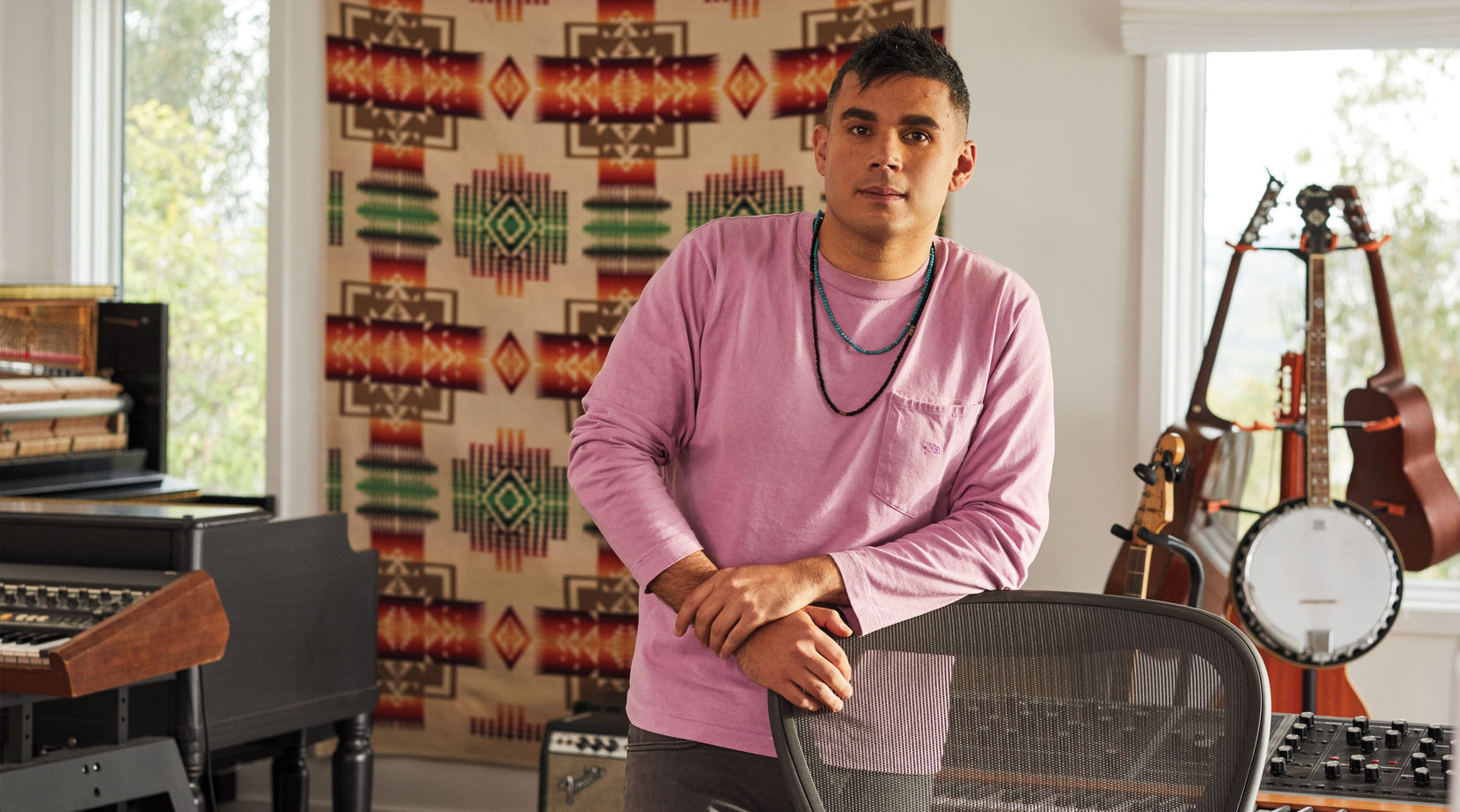 Rostam, musiker, producer og komponist, stod lænet op ad en Aeron-kontorstol i grafit med musikinstrumenter i baggrunden.